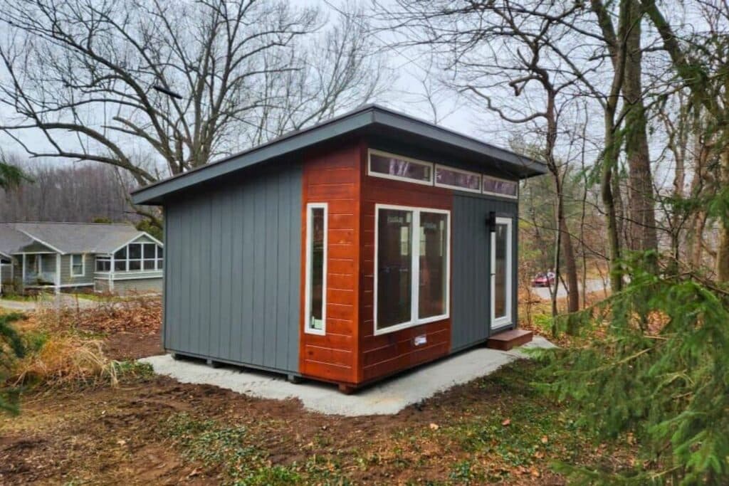 Studio Shed on concrete foundation in wooded yard with home in background