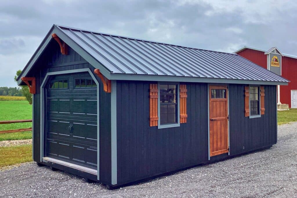 Blue Shed with Garage door and wooden door and widen shutters on gravel road with red barn in background