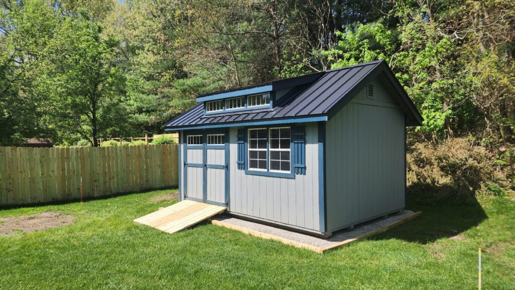 Blue-gray utility shed with black metal roof, double doors, and shutters, for sale